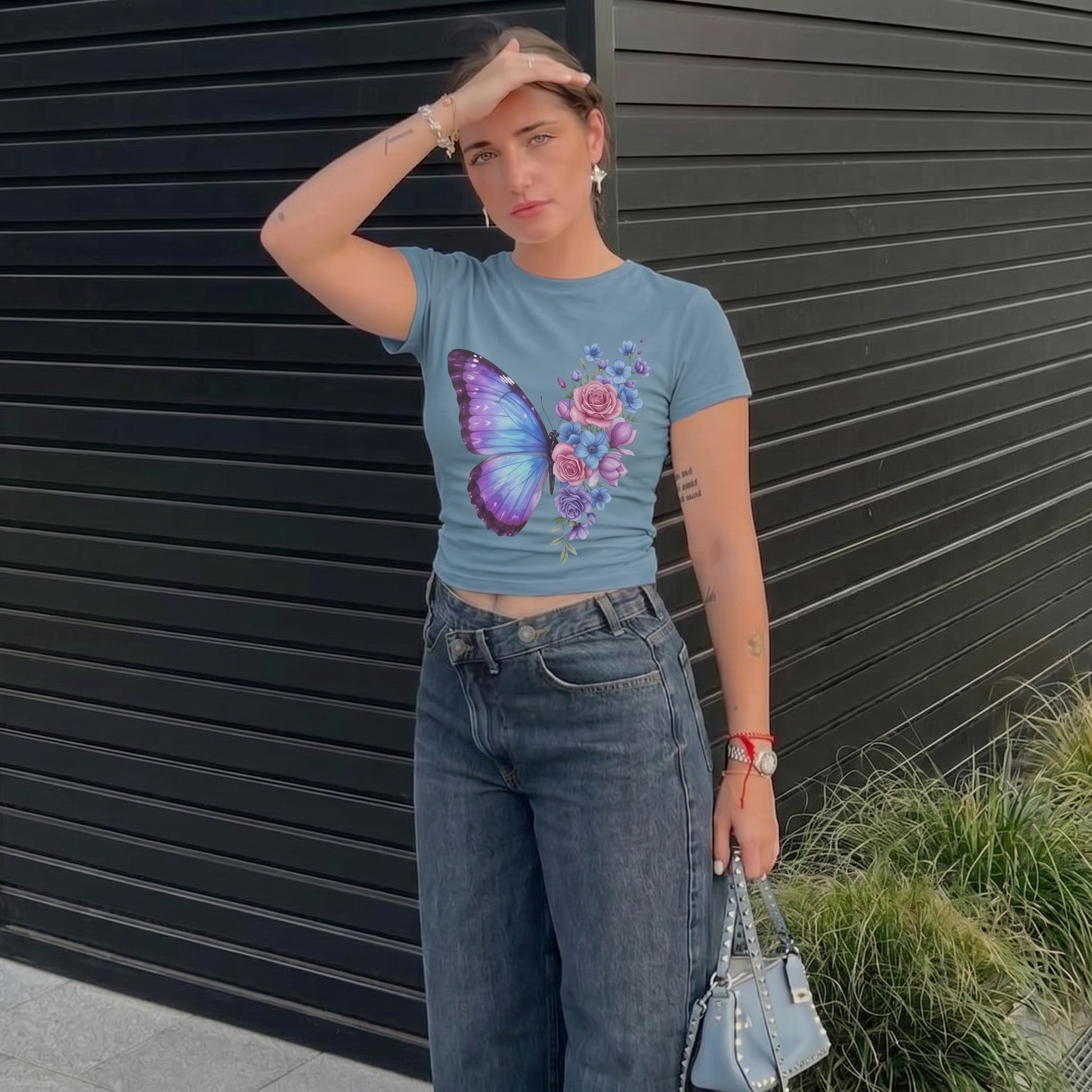 TrendyShift.Com women's blue micro rib baby tee featuring a pastel butterfly and floral print, worn with dark jeans.